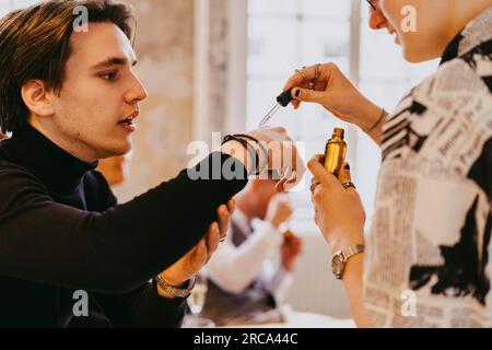 Nicht-binäre Person, die eine ätherische Ölprobe an der Hand eines männlichen Kollegen während einer Veranstaltung im Kongresszentrum testet Stockfoto
