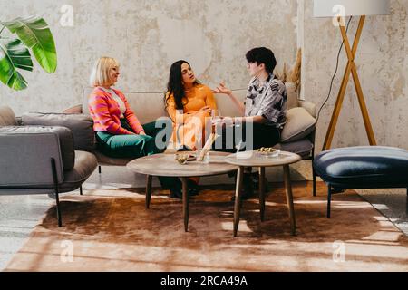 Nicht-binäre Person, die mit weiblichen Kollegen spricht, die während der Veranstaltung im Kongresszentrum auf dem Sofa sitzen Stockfoto