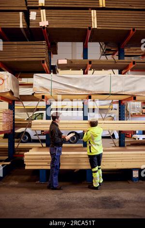 Multirassische weibliche Kollegen mit Brettern auf einem Regal diskutieren während der Arbeit in der Holzindustrie Stockfoto