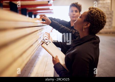 Multirassische weibliche Kollegen, die Bretter auf Regalen in der Holzindustrie untersuchen Stockfoto