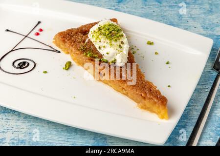 Türkisches Dessert ekmek kadayifi mit Milchcreme und Pistazien auf einem weißen Porzellanteller Stockfoto