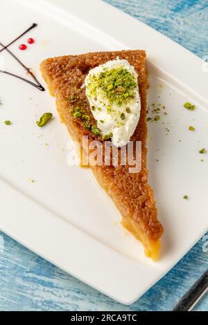 Türkisches Dessert ekmek kadayifi mit Milchcreme und Pistazien auf einem weißen Porzellanteller Stockfoto