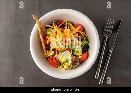 Salat mit Karotten, Tomaten, Mais und vielen Grüns auf einem weißen Porzellanteller Stockfoto
