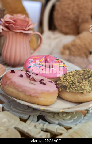 Nahaufnahme von verschiedenen Donuts mit rosa glasierten und bestreuten Donuts und Geschirr Stockfoto