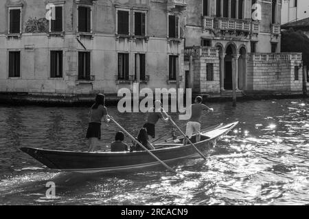 Schwarz & Weiß - Gruppe von Personen, die im venezianischen Reihenstil am Canale Grande bei Sonnenuntergang rudern, Sestiere von Dorsoduro, Venedig, Venetien, Italien Stockfoto