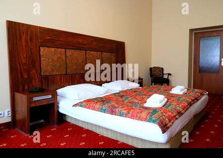 Gemütliches Schlafzimmer im klassischen Vintage-Stil im Haus, Hotel, Apartment, Gästehaus. Doppelbett, weiße Kissen und Bettwäsche, rote Federdecke. Karlsbad, Tschechien Stockfoto