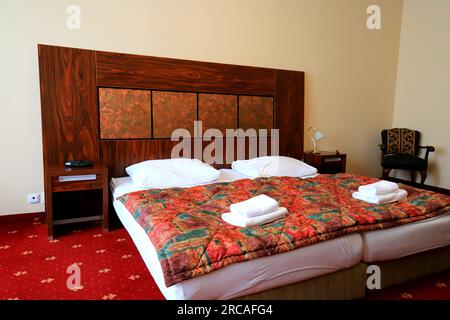 Gemütliches Schlafzimmer im klassischen Vintage-Stil im Haus, Hotel, Apartment, Gästehaus. Doppelbett, weiße Kissen und Bettwäsche, rote Federdecke. Karlsbad, Tschechien Stockfoto