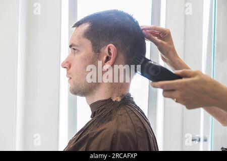 Eine Frau, die einem weißen Mann einen Haarschnitt in einem Heim verpasst. Familienleben und sorgenfreier moderner Lebensstil. Konzept von Komplizenschaft und Vertrauen. Schließen Stockfoto