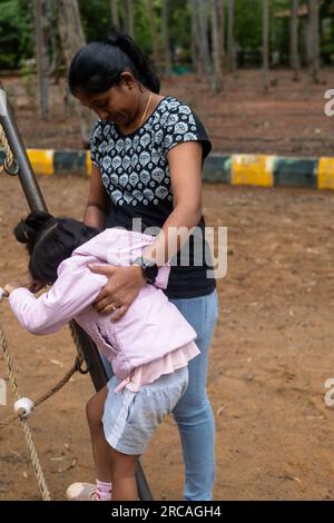 Eine Mutter hilft ihrer kleinen Tochter, ein Seil in einem Park zu erklimmen. Die Mutter hält die Hand der Tochter und ermutigt sie. Stockfoto