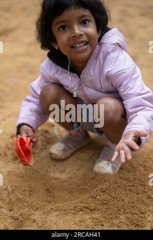 Ein fröhliches kleines Mädchen spielt im Schlamm. Sie ist mit Schlamm bedeckt und hat viel Spaß. Stockfoto