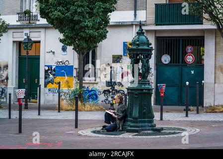 Frau sitzt neben dem Wallace-Brunnen am Pariser Commune Square im beliebten 13. Arrondissement, Paris, Frankreich Stockfoto