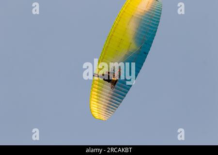 Ein motorisierter Gleitschirm mit blauer und gelber Haube und blauem Himmelshintergrund. Stockfoto