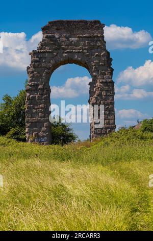 Der beeindruckende antike römische Aquädukt-Bogen steht hoch inmitten der ruhigen Schönheit des Parco degli Acquedotti, eingerahmt von einem Teppich gelber Wildblumen. Stockfoto