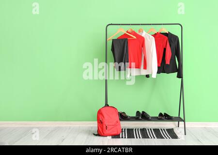 Stilvolle Schuluniform, die an einem Regal, einem Rucksack und Schuhen in der Nähe der grünen Wand im Zimmer hängt Stockfoto