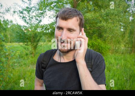Ein bärtiger junger Mann, der im Wald telefoniert Stockfoto