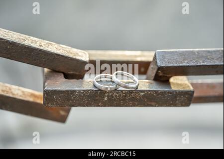 Zwei Hände mit Eheringen liegen auf einer starken Ankerkette. Stockfoto