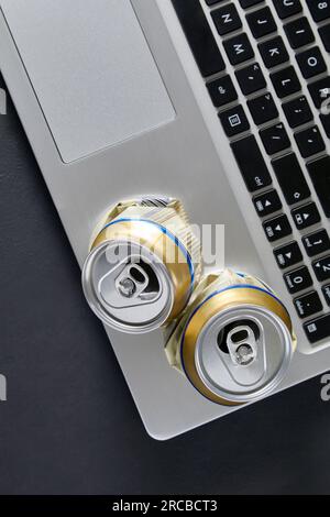 Leere zerknitterte Bierdosen auf der Laptop-Tastatur auf schwarzem Hintergrund. Betrunkene Kämpfe in sozialen Medien. Scheidungsgrund in der Familie. Stockfoto