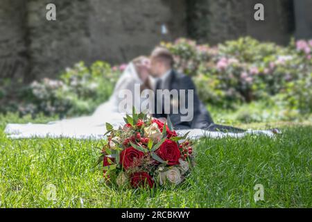 Hochzeitsstrauß im Vordergrund eines verschwommenen küssenden Paares. Blumen und Liebhaber. Stockfoto