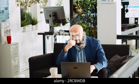 Der Analyst des Unternehmens denkt über einen Strategieplan nach und schreibt Daten auf einem Laptop in Großraumbüros. Business Manager sammeln Ideen für Projekte der Geschäftsleitung, bevor sie eine neue Entwicklungsvision entwickeln. Stativaufnahme. Stockfoto