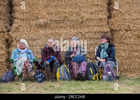 Eine Gruppe von Frauen saß neben einer Reihe Strohballen, während sie auf einem weißen Metallstuhl saßen und an einem kühlen Abend Livemusik hörte. Stockfoto