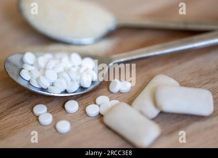 Leipzig, Deutschland. 12. Juli 2023. Ein Löffel voller Süßmitteltabletten liegt neben einem Löffel voller Zucker und Kaugummi mit Süßstoffen. Ein Süßungsmittel, das häufig in Erfrischungsgetränken, Joghurt und Kaugummi verwendet wird, kann nach einer neuen Expertenklassifikation möglicherweise Krebs beim Menschen verursachen - aber es sollte kein Problem in den häufig verzehrten Mengen sein. Es geht um Aspartam, eines von elf in der EU zugelassenen Süßungsmitteln. (Zu dpa 'Süßungsmittel Aspartam könnte Krebs verursachen - mäßiger Konsum harmlos') Kredit: Hendrik Schmidt/dpa/Alamy Live News Stockfoto