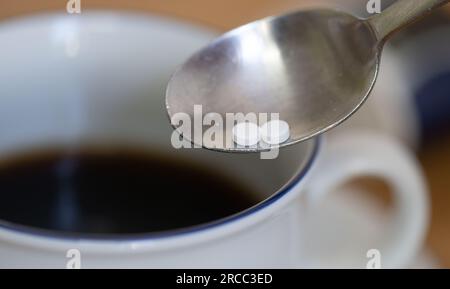 Leipzig, Deutschland. 12. Juli 2023. Über einer Tasse Kaffee ist ein Löffel mit zwei Süßstofftabletten zu sehen. Ein Süßungsmittel, das häufig in Erfrischungsgetränken, Joghurt und Kaugummi verwendet wird, kann nach einer neuen Expertenklassifikation möglicherweise Krebs beim Menschen verursachen - aber es sollte kein Problem bei den häufig verzehrten Mengen sein. Es geht um Aspartam, eines von elf in der EU zugelassenen Süßungsmitteln. (Zu dpa 'Süßungsmittel Aspartam könnte Krebs verursachen - mäßiger Konsum harmlos') Kredit: Hendrik Schmidt/dpa/Alamy Live News Stockfoto