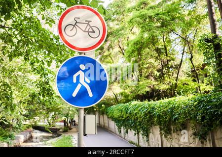 Fahrrad- und Fußgängerschilder im Sommer. Italien. Blick auf ein generisches Schild „Fahrradrennen verboten“ auf einem Fußgängerweg. Das „kein Radfahren“-Zeichen bedeutet, dass die Verwendung von verwendet wird Stockfoto