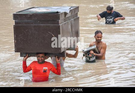 Neu-Delhi, Indien. 12. Juli 2023. Die Menschen tragen ihre Sachen, während sie durch überschwemmtes Wasser in einem tiefliegenden Gebiet waten, nachdem sie durch steigende Wasserstände im Yamuna-Fluss nach heftigen Monsunregen in Neu-Delhi vertrieben wurden. Der Wasserstand von Yamuna in Delhi erreicht eine einmalige Höhe von 207,55 Metern. Die Regierung warnte vor Überschwemmungen und bat die Bewohner des Flussbetts und der tief liegenden Gebiete, ihre Häuser zu evakuieren. (Foto: Biplov Bhuyan/SOPA Images/Sipa USA) Guthaben: SIPA USA/Alamy Live News Stockfoto