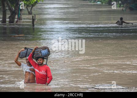 Neu-Delhi, Indien. 12. Juli 2023. Die Menschen tragen ihre Sachen, während sie durch überschwemmtes Wasser in einem tiefliegenden Gebiet waten, nachdem sie durch steigende Wasserstände im Yamuna-Fluss nach heftigen Monsunregen in Neu-Delhi vertrieben wurden. Der Wasserstand von Yamuna in Delhi erreicht eine einmalige Höhe von 207,55 Metern. Die Regierung warnte vor Überschwemmungen und bat die Bewohner des Flussbetts und der tief liegenden Gebiete, ihre Häuser zu evakuieren. (Foto: Biplov Bhuyan/SOPA Images/Sipa USA) Guthaben: SIPA USA/Alamy Live News Stockfoto
