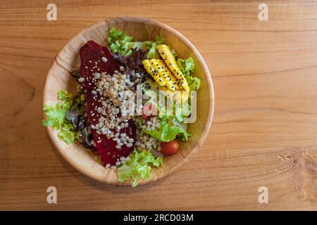 Frisches Gemüse und Obstsalat mit Mais, Rote Bete, Hirse, Salat, Tomaten in einer Holzschüssel auf einem Holztisch. Stockfoto