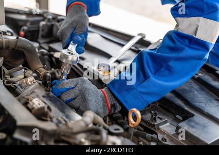 Nahaufnahme der Hände eines männlichen Automechanikers mit einem Netzschlüssel bei der Arbeit am Motor des Autos Stockfoto