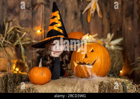 Süßes kleines Hexenmädchen, das in der halloween-Landschaft posiert. Halloween-Party Stockfoto