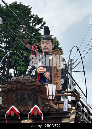 14. Juli 2023, Japan, Sawara: Auf riesigen Holzrädern und begleitet von traditioneller Flöten- und Trommelmusik ziehen Hunderte von Japanern mächtige Wagen durch eine alte Handelsstadt beim Sawara Grand Festival, einem der größten Volksfeste in der Kanto-Region um Tokio. Zu Beginn des dreitägigen Sawara Grand Festivals schubsten und zogen Festivalteilnehmer in traditionellen Kostümen die „Dashi“-Wagen aus dekoriertem Holz, auf denen kostbare Meter hohe Gottheiten, berühmte Samurai oder sogar Tiere verzaubert wurden, und sangen fröhlich durch die Gassen der Altstadt Stockfoto