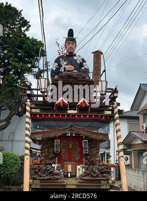 14. Juli 2023, Japan, Sawara: Auf riesigen Holzrädern und begleitet von traditioneller Flöten- und Trommelmusik ziehen Hunderte von Japanern mächtige Wagen durch eine alte Handelsstadt beim Sawara Grand Festival, einem der größten Volksfeste in der Kanto-Region um Tokio. Zu Beginn des dreitägigen Sawara Grand Festivals schubsten und zogen Festivalteilnehmer in traditionellen Kostümen die „Dashi“-Wagen aus dekoriertem Holz, auf denen kostbare Meter hohe Gottheiten, berühmte Samurai oder sogar Tiere verzaubert wurden, und sangen fröhlich durch die Gassen der Altstadt Stockfoto