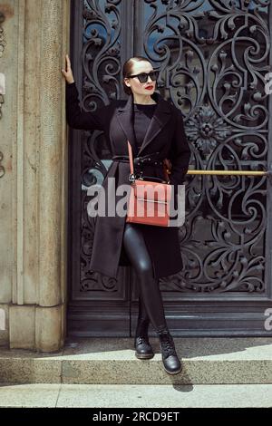Junge Frau in Schwarz, die vor einer schwarzen Tür steht Stockfoto