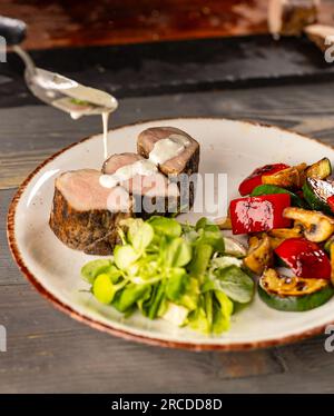 Der Koch gießt den Salat aus einem Löffel mit Soße. Stockfoto