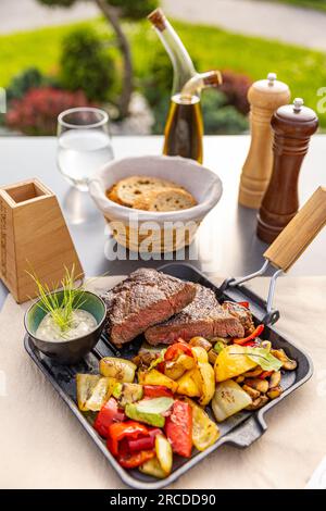 Gegrillte Schweinekoteletts mit geröstetem Gemüse, serviert mit Sauce in einer Eisentasse, Restaurantmenü Stockfoto