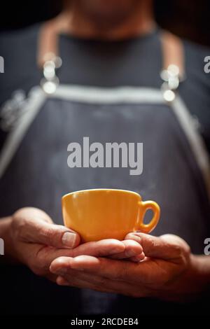 ein weißer Mann, der mit beiden Händen eine orangefarbene Tasse Kaffee hält. Speicherplatz kopieren Stockfoto