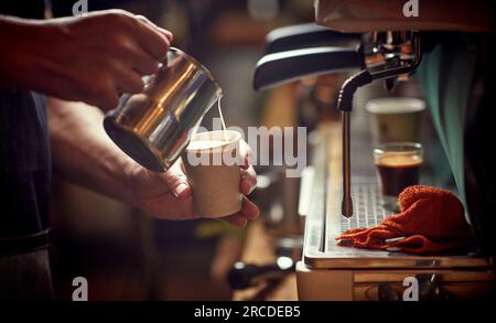 weiße männliche Hände, die Milch in einen Kaffee in einem Pappbecher gießen. Nahaufnahme Stockfoto