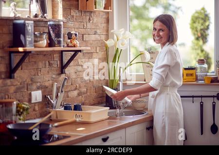 Horizontale Aufnahme einer jungen Frau, die in einer modernen Küche Geschirr spült und Freude empfindet. Lifestyle, Heimkonzept. Stockfoto