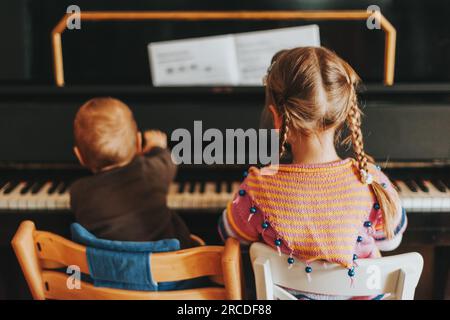 Zwei kleine Kinder spielen auf Klavier, ein kleines Mädchen und ein kleiner Junge üben zu Hause Musik, Rückansicht Stockfoto