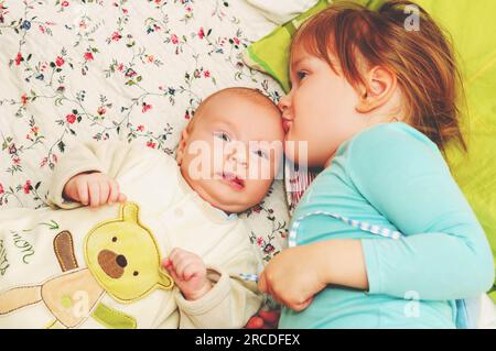 Ein kleines Mädchen küsst ihren kleinen Bruder, Kinder spielen zusammen Stockfoto