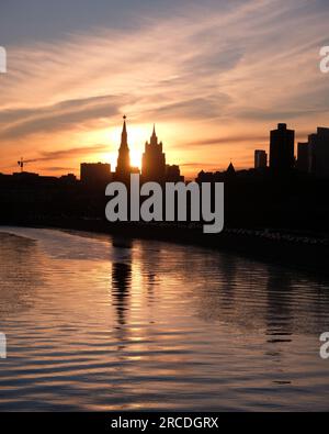 Stadtlandschaft mit Moskauer Fluss, Ufer und Silhouetten von Gebäuden und Kreml Türmen im purpurroten Sonnenuntergang Stockfoto