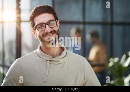 Mein Team zum Erfolg führen. Attraktiver junger Geschäftsmann in eleganter Freizeitkleidung, der die Arme überkreuzt und lächelt Stockfoto