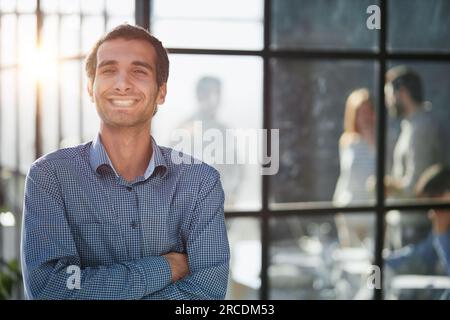 Weißer Mann mittleren Alters, kreativ in legerer Bürolounge, mit Blick auf die Kamera, Arme überkreuzt, Taille nach oben Stockfoto