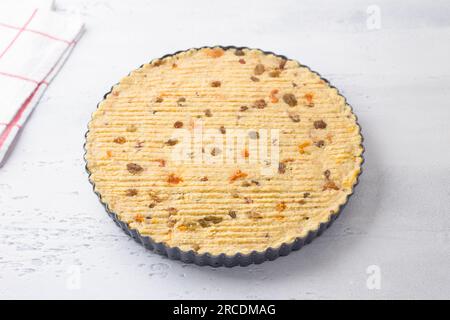 Hirse-Auflauf mit Nüssen und getrockneten Früchten in einer Backform, roh, auf hellblauem Hintergrund. Sie kochen ein köstliches veganisches Gericht, Schritt für Schritt. Stockfoto