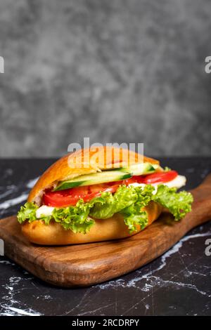 Sandwich mit Käse, Tomaten, Gurke und Salat. Köstliches Sandwich auf dem Servierbrett aus Holz Stockfoto