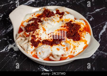 Ravioli mit Sauce und Joghurt. Ravioli auf dunklem Hintergrund. Türkische Köstlichkeiten. Schließen Stockfoto