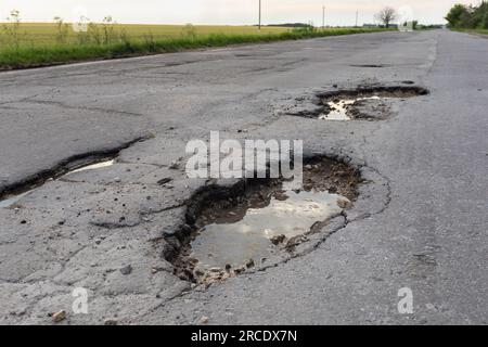 Gruben auf der Asphaltstraße, ein Konzept zum Thema schlechte Straßen Stockfoto