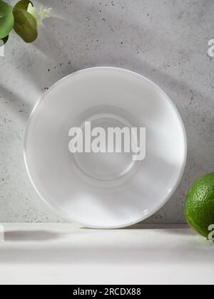 Weiße Keramikplatte auf abstraktem Hintergrund, umgeben von Blumen und Kalk Stockfoto